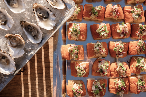 Oysters on a half shell with small sandwiches on a blue surface