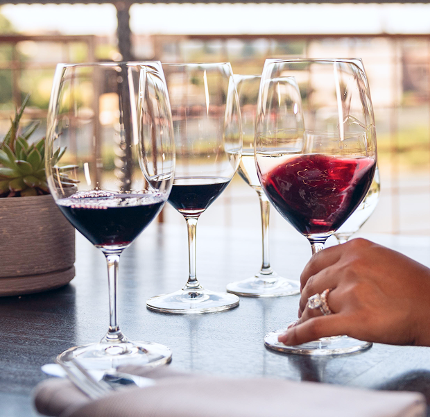 Table with multiple glasses of red and white wine on it and a woman swirling a glass of red wine