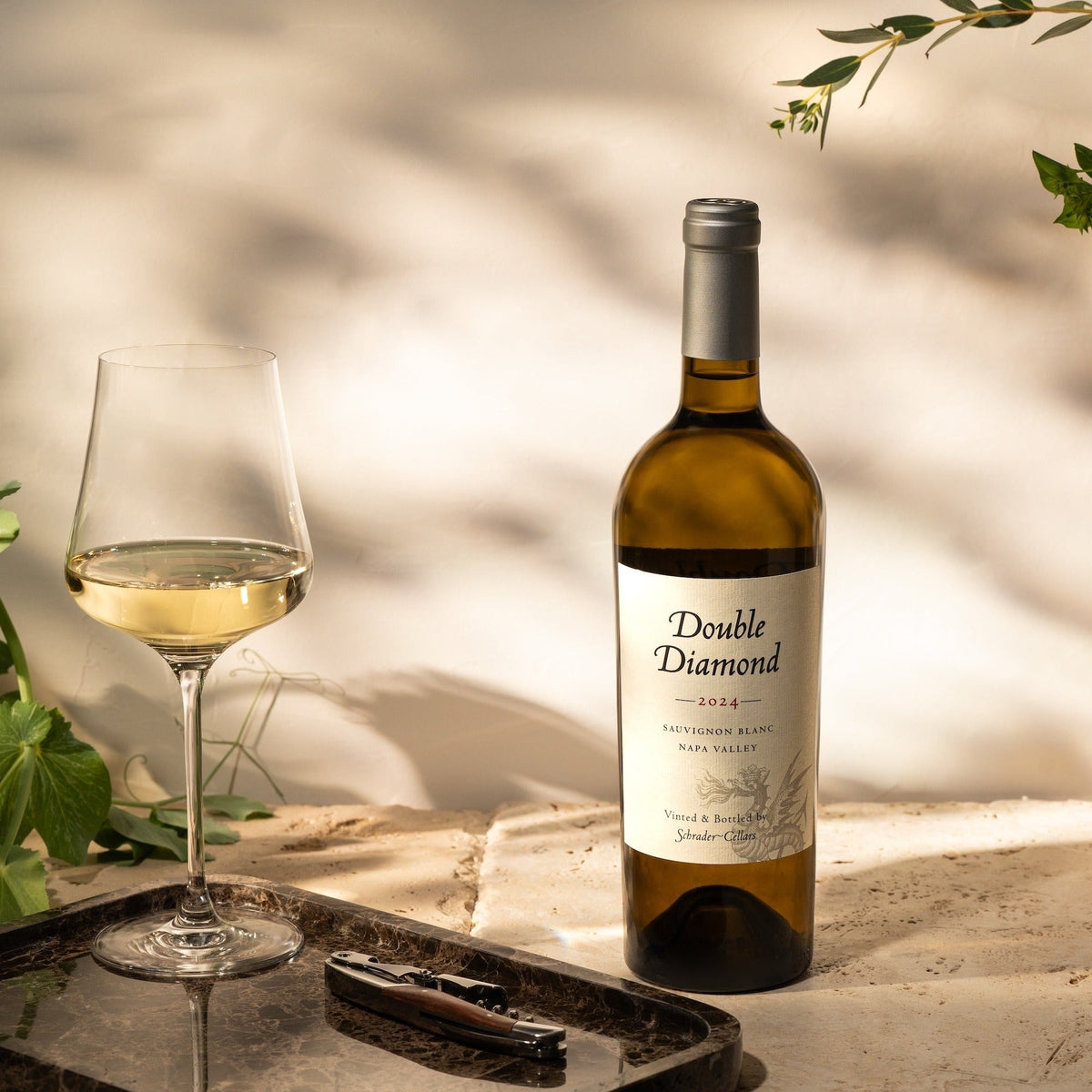 Bottle of Double Diamond wine with a glass on a tray, surrounded by plants.