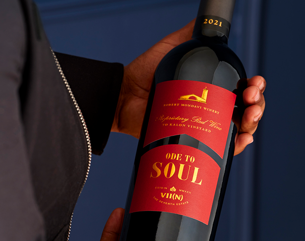 Person holding a bottle of Ode to Soul Red Wine with a blue background 