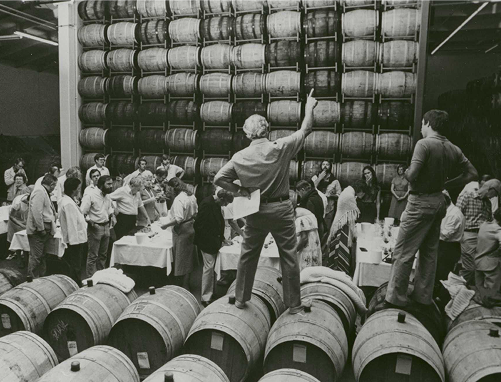 Old black and white picture of men working in a room full of wine barrels
